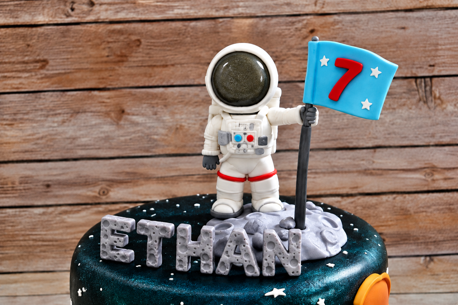 Space-themed cake with an edible white astronaut topper holding a blue flag with the number 7 above the name Ethan.