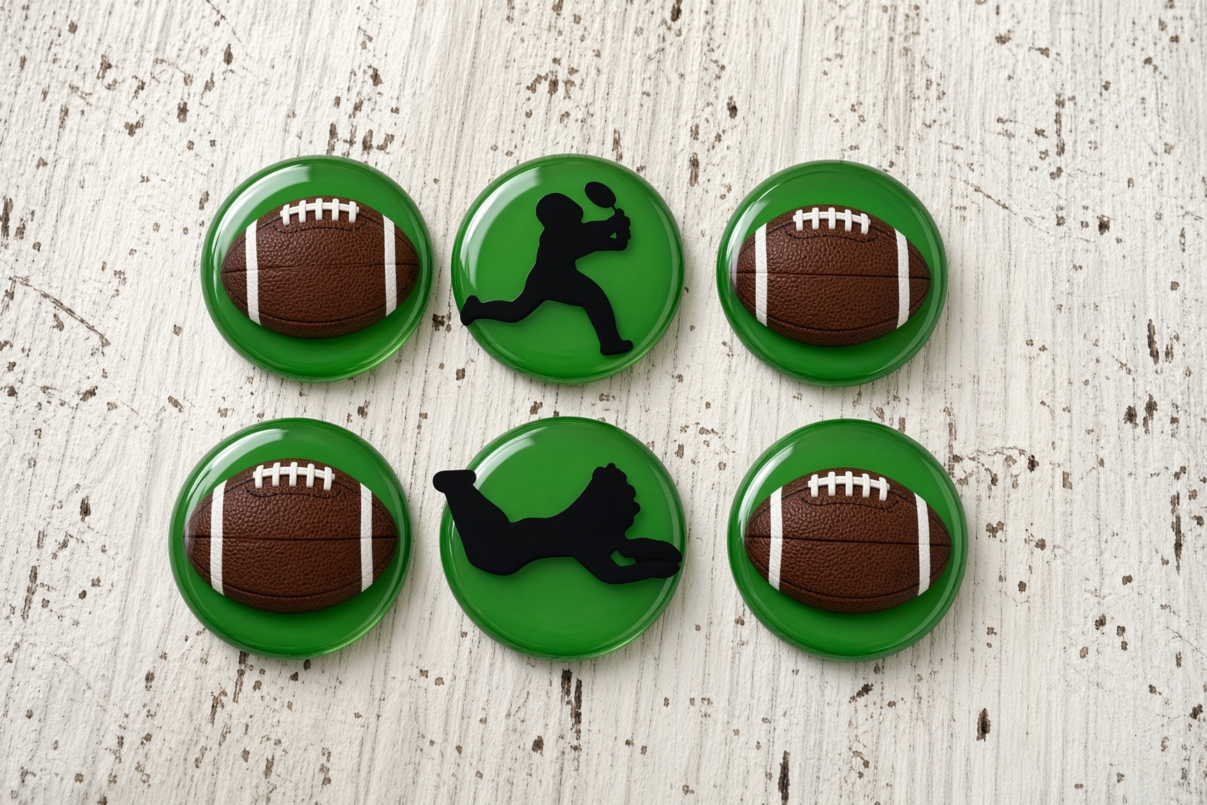 Six green edible football cupcake toppers—four footballs and two player silhouettes—arranged on a white wood surface.